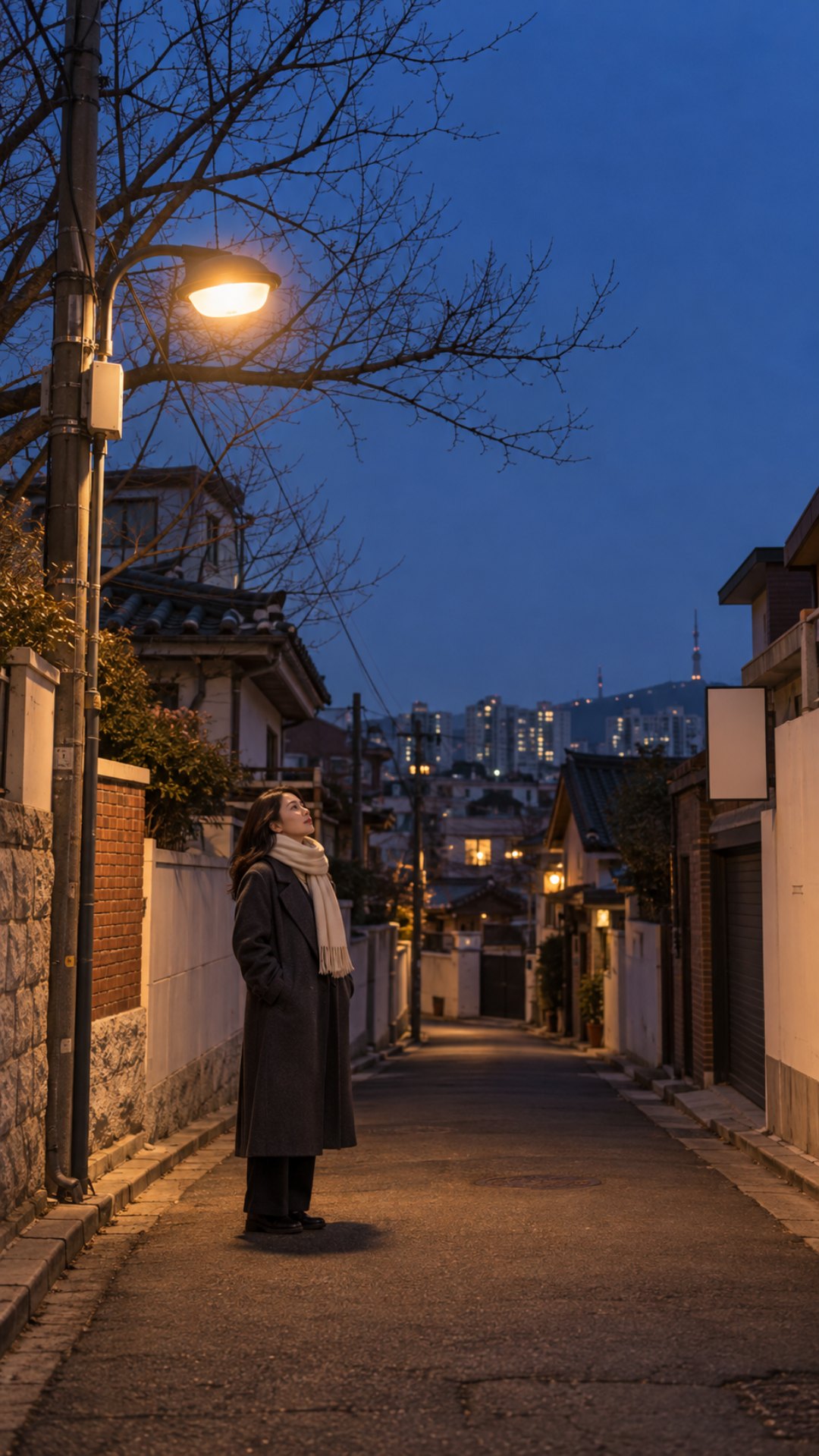 눈이 오기 전 마른 바닥의 겨울 저녁 골목, 가로등 아래 회색 코트를 입은 지어낸 30대 여성이 서 있는 세로 그림